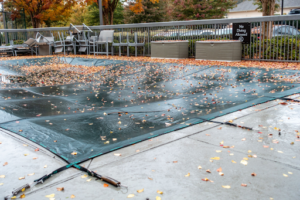 A pool with a cover on it and dead leaves on top of it.
