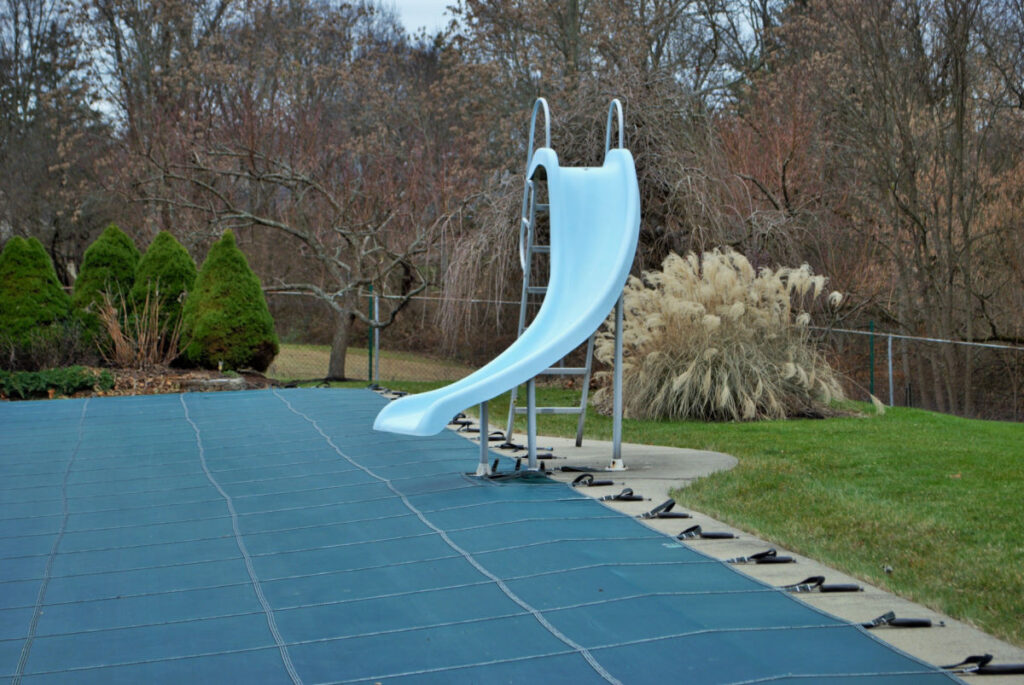 A slide near a closed pool with a cover on it.