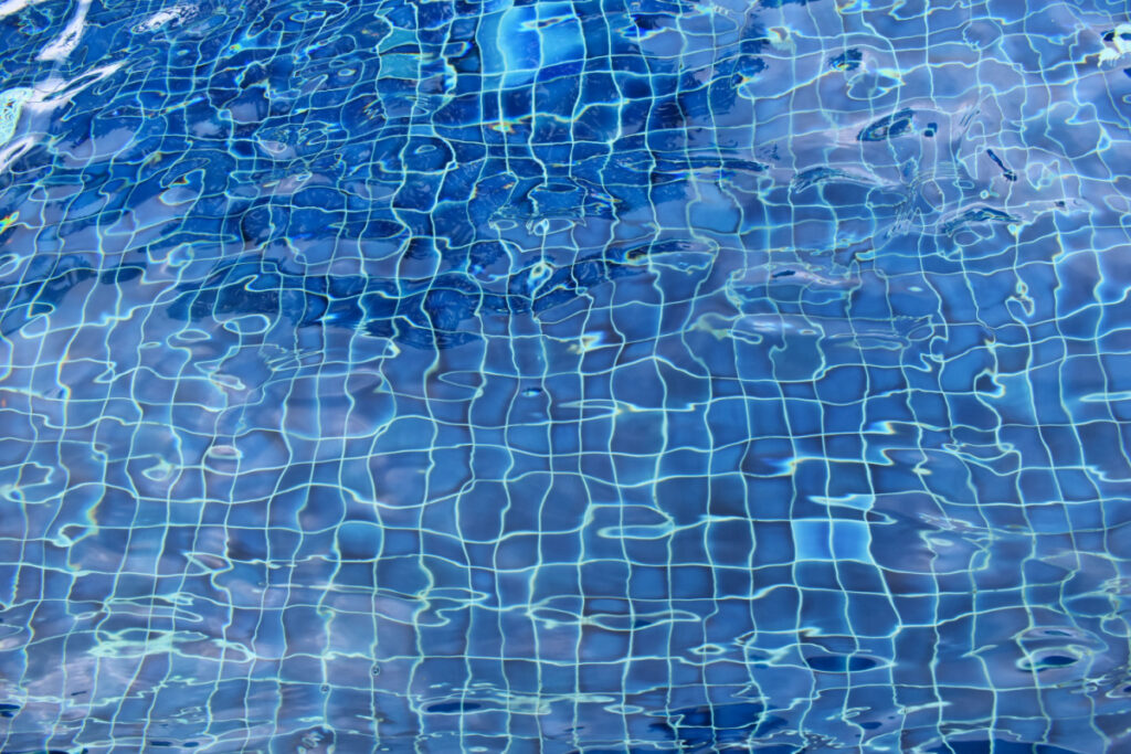 The rippling surface of water in a pool with a blue pattern beneath the surface.